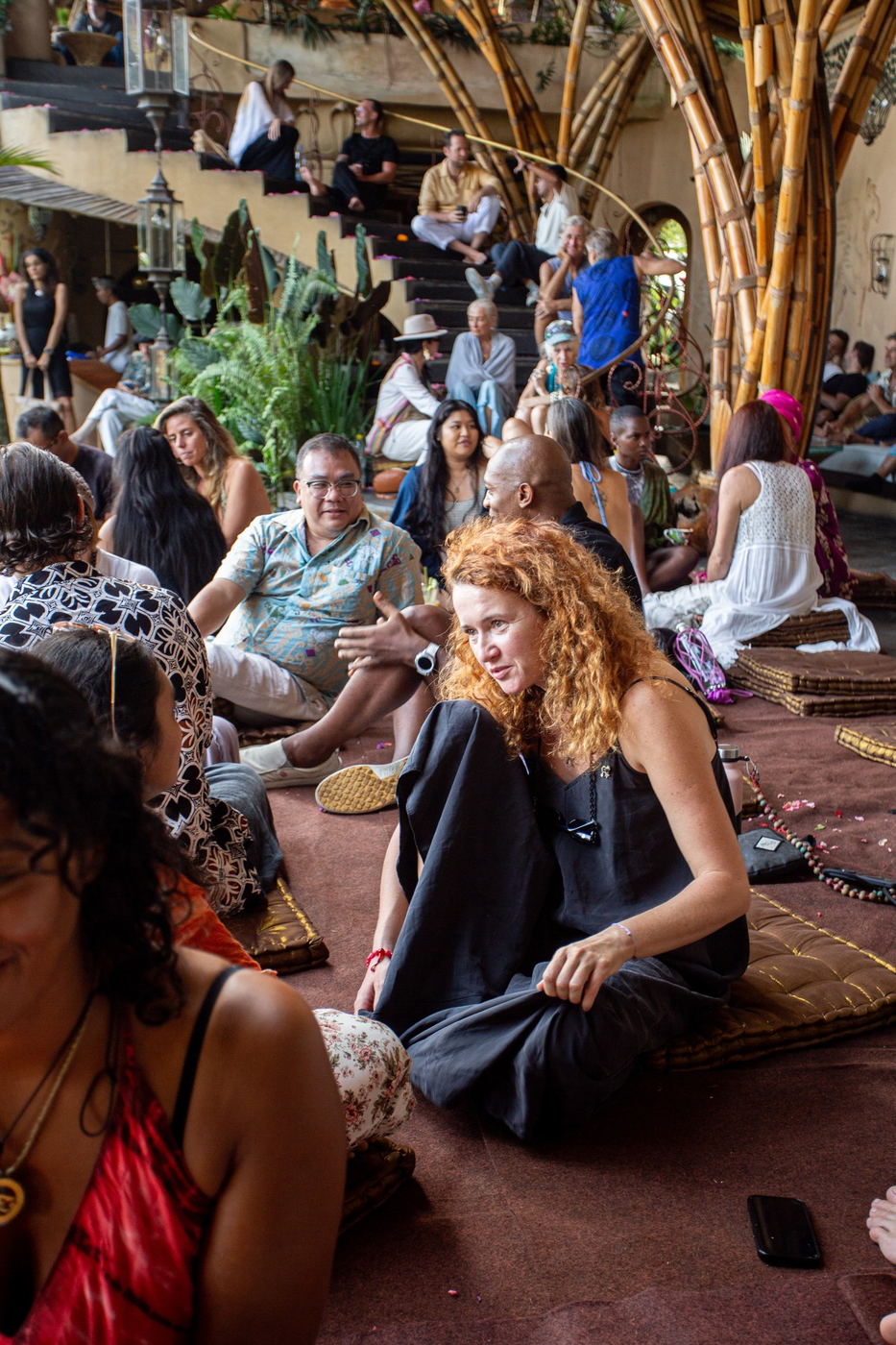 Wide shot of the crowd seated on cushions, listening