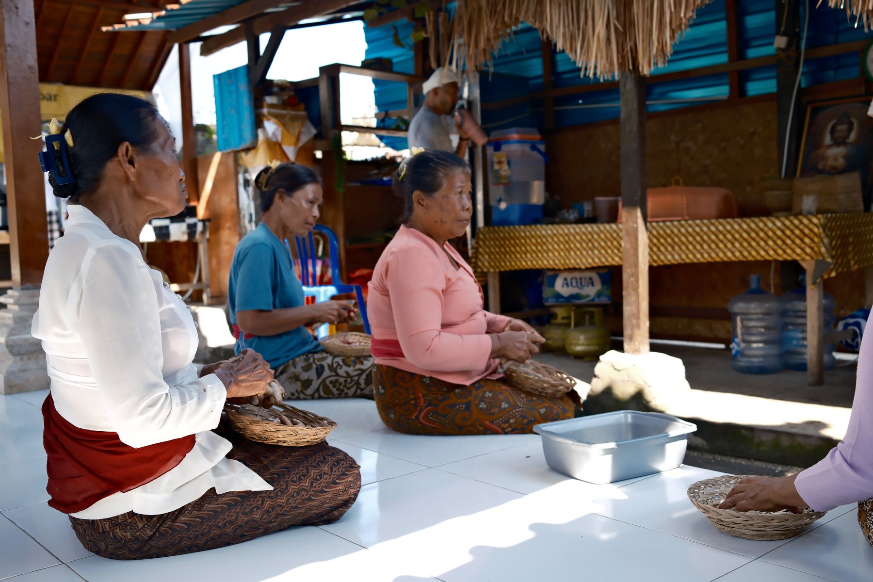 Three women peeling spices into woven baskets on the tiled floor