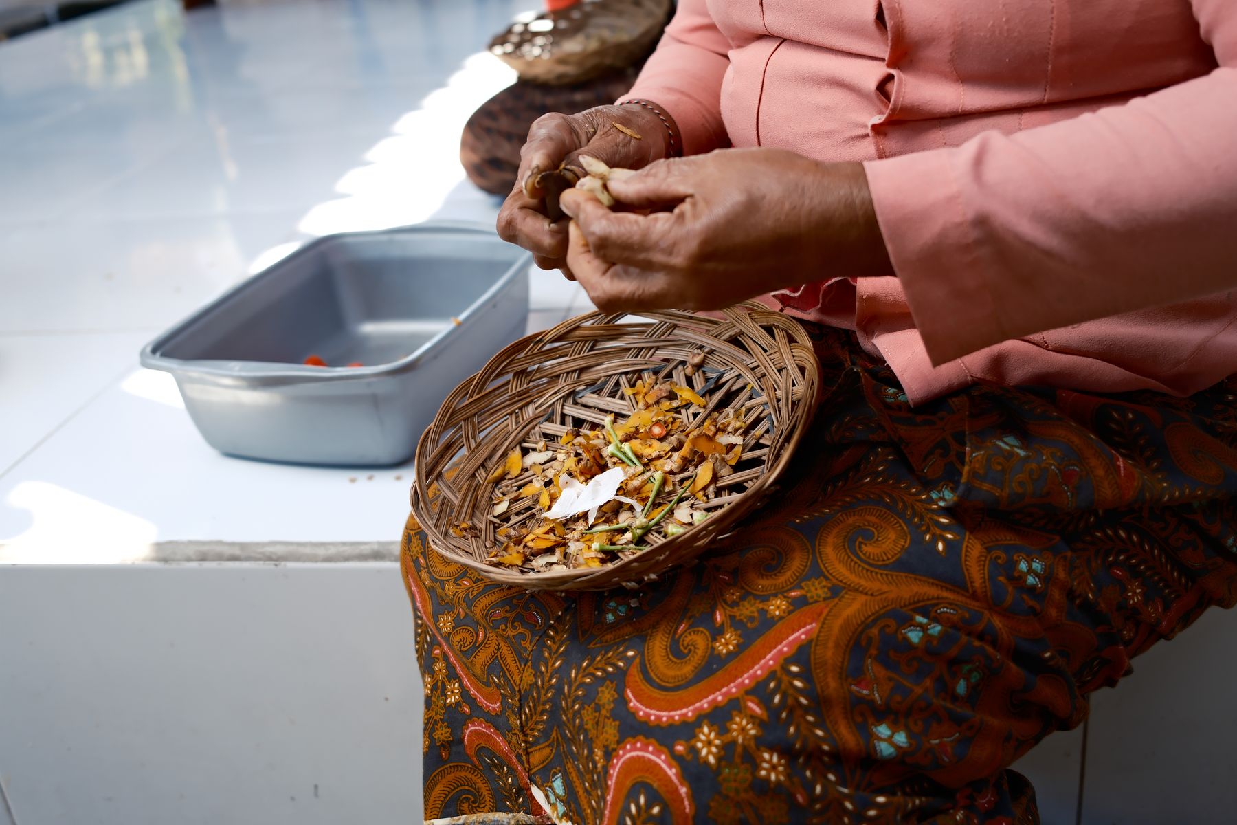 Hands snapping ginger above a basket of turmeric shavings and chillies