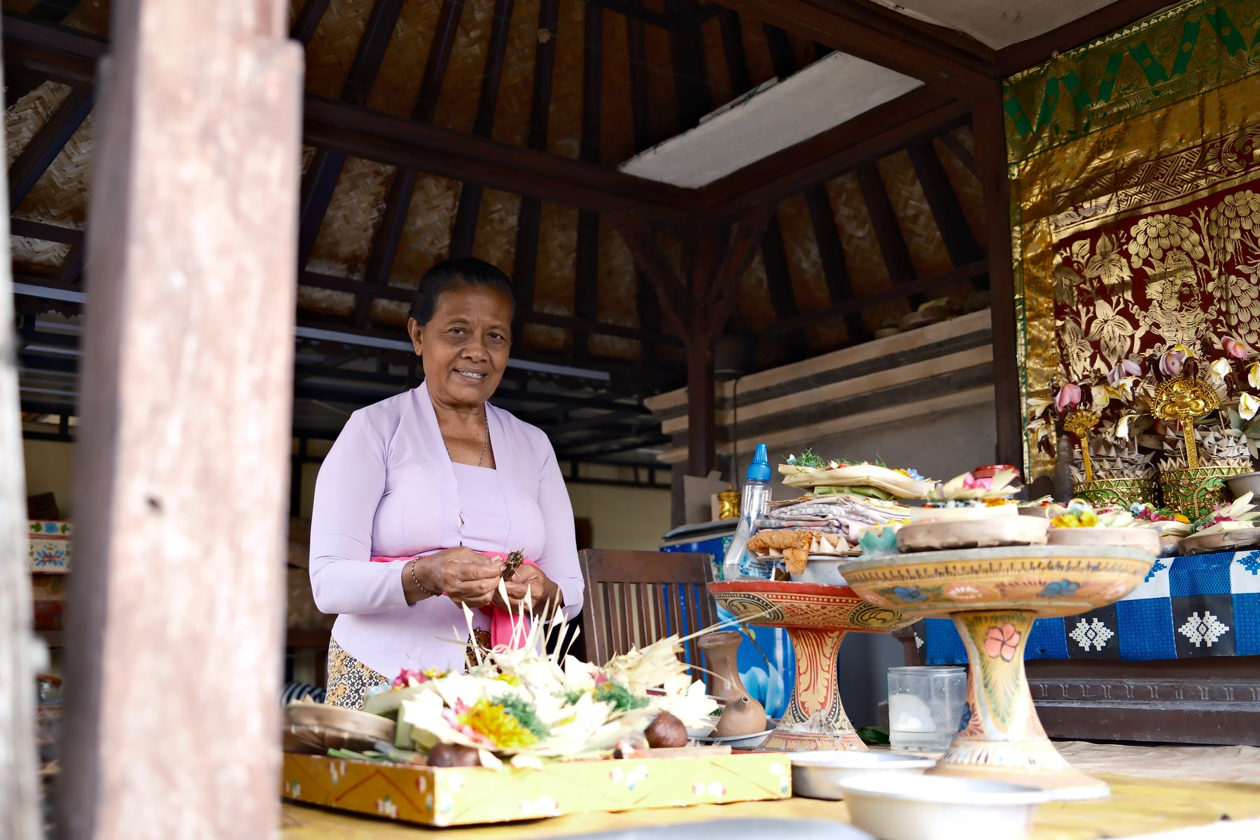 A woman assembles palm-leaf offerings in the family temple pavilion