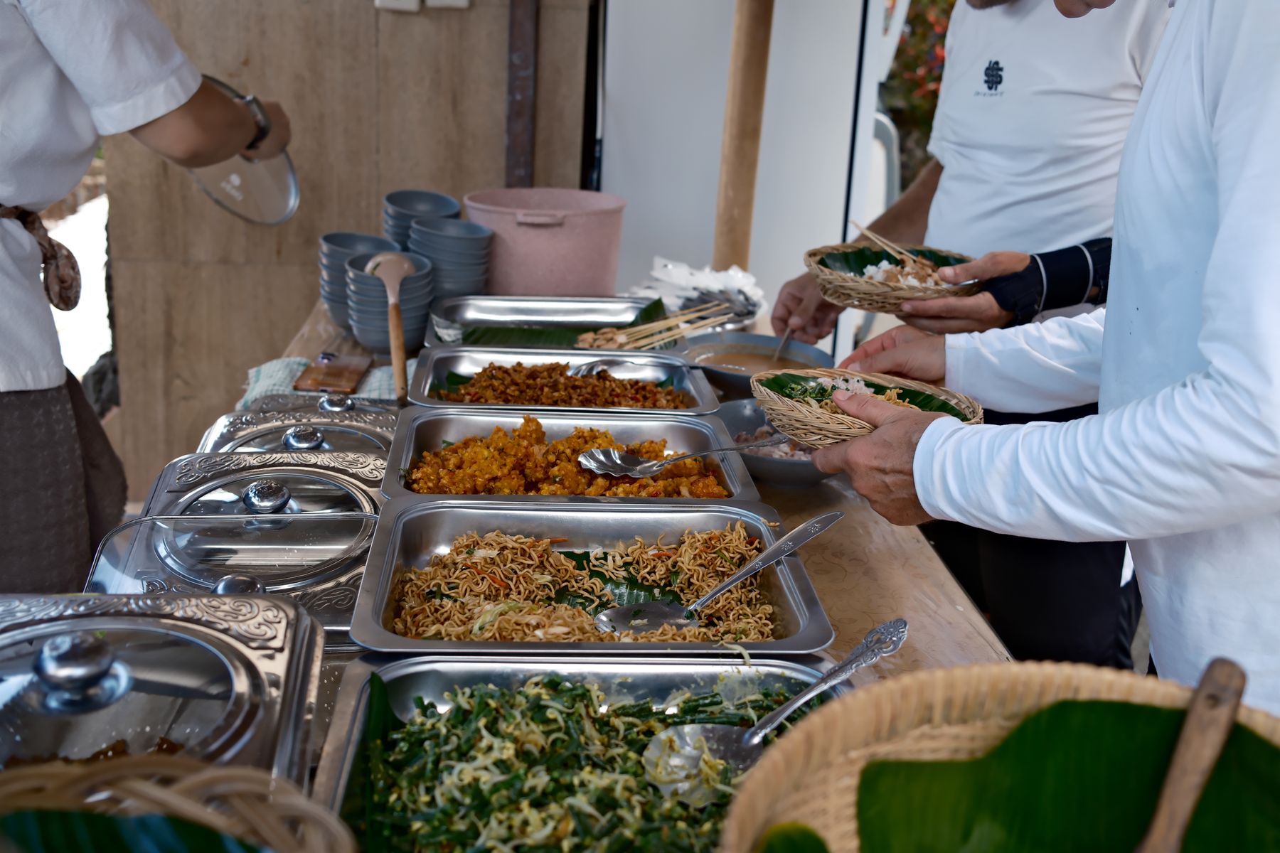 Guests fill woven banana-leaf baskets from trays of Balinese dishes