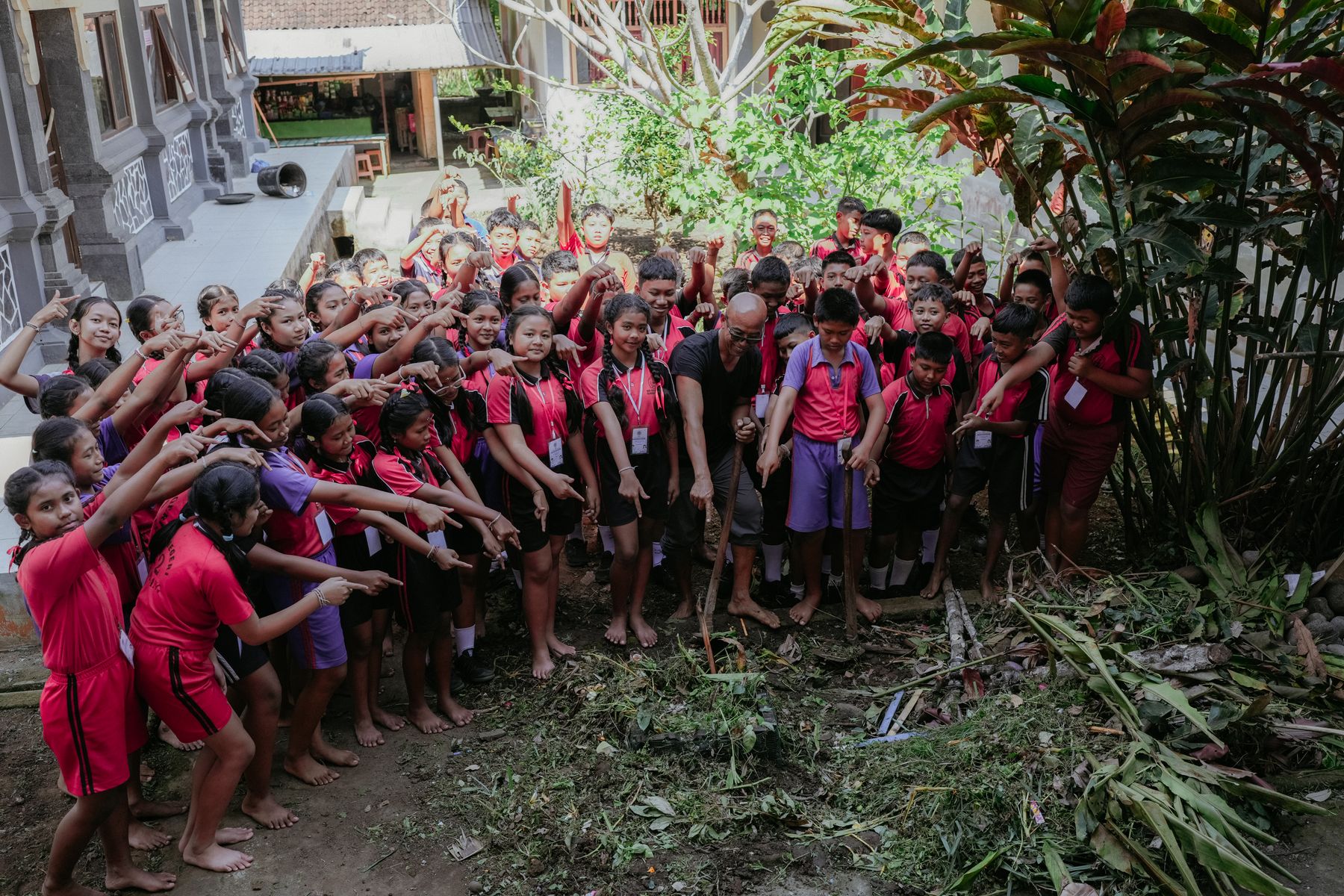 Pupils gesturing toward garden clippings collected beside the school building